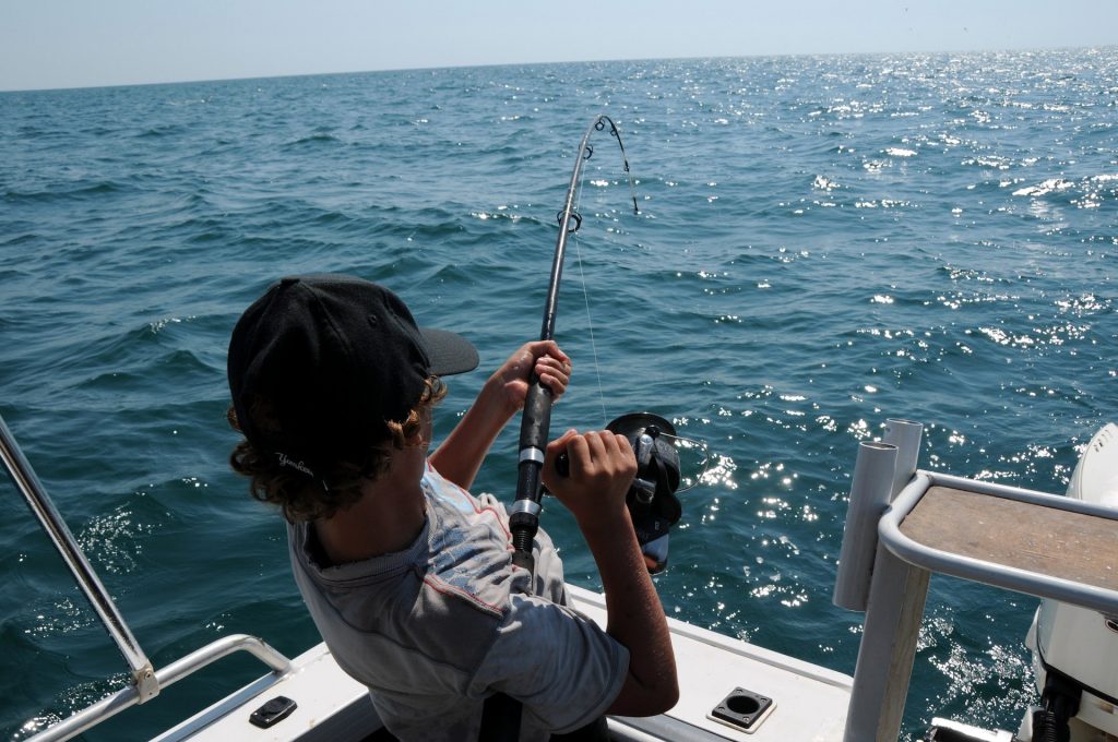 man on boat reeling in caught fish with rod and line